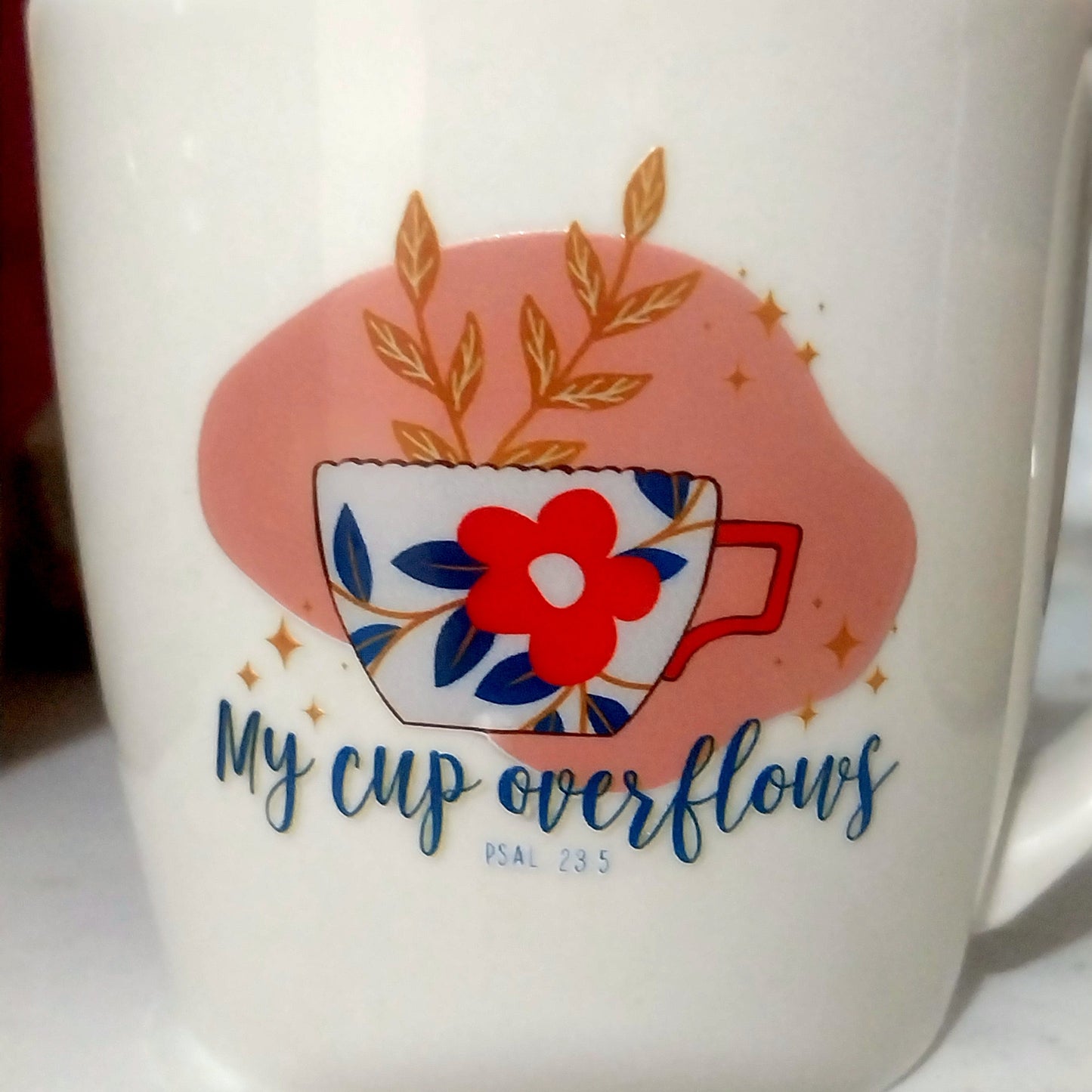 Mug with floral design and text 'My cup overflows' on a white surface